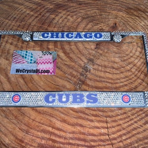 May include: A silver license plate frame with clear rhinestones and blue and red accents. The frame says "CHICAGO CUBS" with the Chicago Cubs logo on each side.