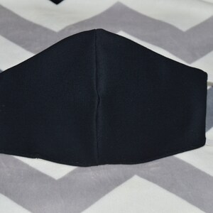 May include: A black face mask with white elastic ear loops. The mask is made of a soft, breathable fabric.