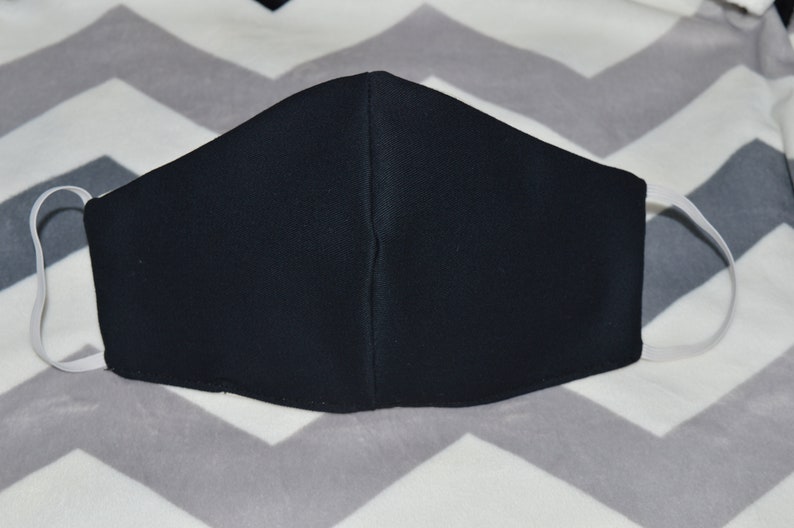 May include: A black face mask with white elastic ear loops. The mask is made of a soft, breathable fabric.