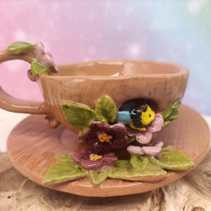 Può includere: Un set di tre tazze in ceramica color crema con smalto maculato. Ogni tazza presenta un diverso motivo floreale dipinto a mano nei toni del blu, verde e giallo. Le tazze hanno una forma semplice e arrotondata.