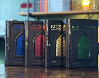 May include: Four hardcover books with black covers and gold lettering. The titles are "Eragon", "Eldest", "Brisinger", and "Inheritance: Inheritance Cycle Book Four". The books are part of the Inheritance Cycle series by Christopher Paolini.