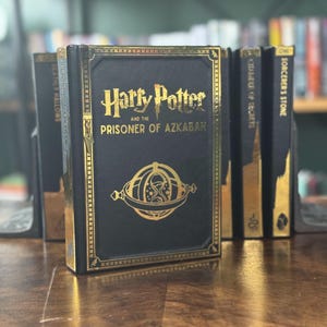 May include: A black leather-bound book with gold lettering and a gold design on the cover. The title is "Harry Potter and the Prisoner of Azkaban".