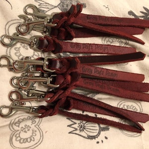 May include: A set of eight maroon leather keychains with silver swivel clips. Each keychain has the text "Grey Dog's Design" embossed on the leather.