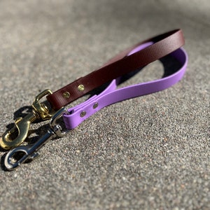 May include: Two dog leashes, one brown leather and one purple rubber, with gold and silver clasps.