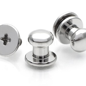 May include: Three silver metal push button fasteners with a round head and a flat base. The fasteners have a cross-shaped slot for a screwdriver.