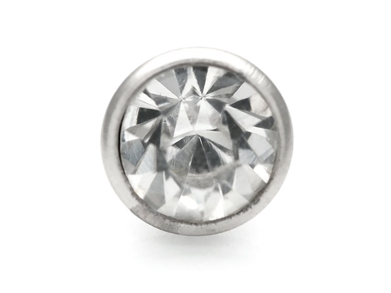 May include: A clear, faceted gemstone set in a silver bezel. The gemstone is round and has a high polish.