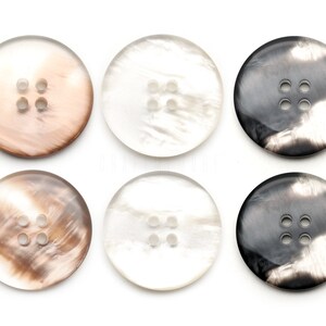 以下が含まれることがあります： 茶色、白、黒の様々な色合いの、丸い4つ穴のボタンが6つ。ボタンは、まだら模様で、大理石のような外観です。