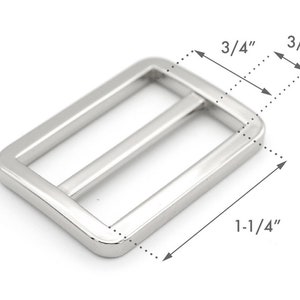 K&ouml;nnte beinhalten: Silberfarbener Metallschnalle mit rechteckiger Form und zwei parallelen Balken. Die Schnalle misst 3,18 cm x 1,91 cm.