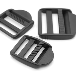 May include: Three black plastic slider buckles. The buckles have two slots and a textured surface.