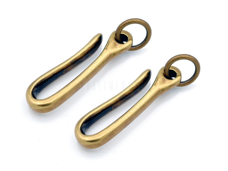 Pode incluir: Dois chaveiros de lat&atilde;o com um design de gancho. Cada chaveiro tem um anel redondo na parte superior.