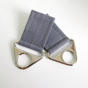 May include: Two gray fabric loops with silver metal rings. The loops are sewn with a straight stitch and the rings are attached to the loops.
