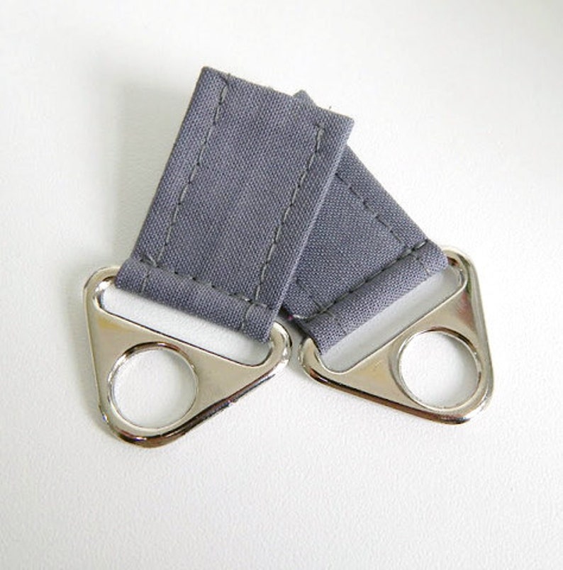May include: Two gray fabric loops with silver metal rings. The loops are sewn with a straight stitch and the rings are attached to the loops.