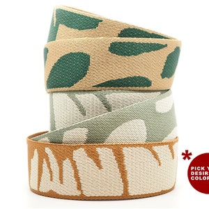 Puede incluir: Tres rollos de tejido elástico con diferentes patrones. El rollo superior es de color beige con diseños de hojas verdes. El rollo del medio es de color gris claro con diseños de hojas beige. El rollo inferior es de color beige con diseños de hojas blancas. El texto "¡Elige tu color deseado!" está en un círculo rojo.