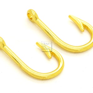 May include: Two gold-colored metal hooks. The hooks are in the shape of a fish hook.