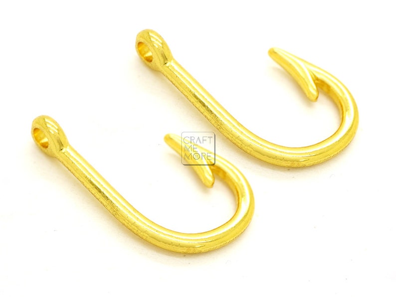 May include: Two gold-colored metal hooks. The hooks are in the shape of a fish hook.