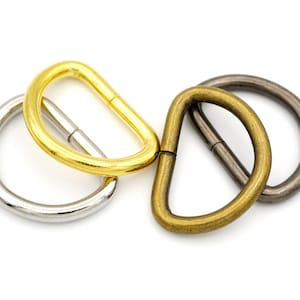 May include: Three metal D-rings in different finishes: gold, brass, and silver. The rings are all the same size and shape.