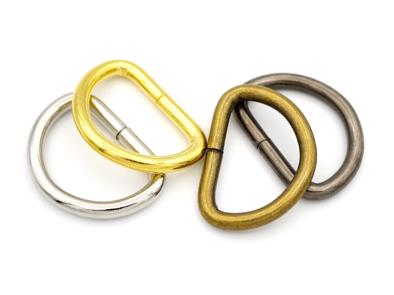 May include: Three metal D-rings in different finishes: gold, brass, and silver. The rings are all the same size and shape.