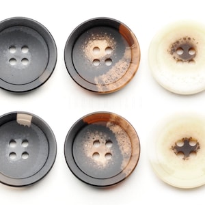 以下が含まれることがあります： 茶色と黒のまだら模様と茶色と白のまだら模様の丸いボタンが6つ。ボタンには穴が4つあります。