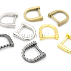 May include: Assortment of six metal D-rings in various finishes, including silver, gold, black, and brass. The D-rings are all the same size and shape.
