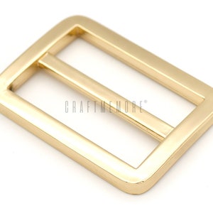 K&ouml;nnte beinhalten: Goldene Metallschnalle mit rechteckiger Form und einem einzigen Querbalken in der Mitte. Die Schnalle ist f&uuml;r die Verwendung mit Riemen oder G&uuml;rteln konzipiert.
