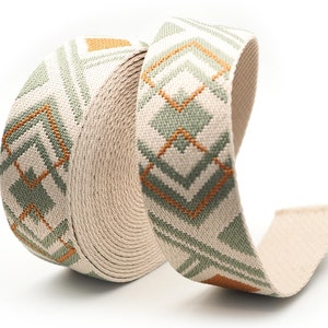 K&ouml;nnte beinhalten: Eine Rolle beiges Stoffband mit einem geometrischen Muster in Gr&uuml;n- und Oranget&ouml;nen. Das Band ist eng gewickelt und zeigt die detaillierte Webart und das Design. Das Muster zeigt Diamanten- und Chevron-Formen.