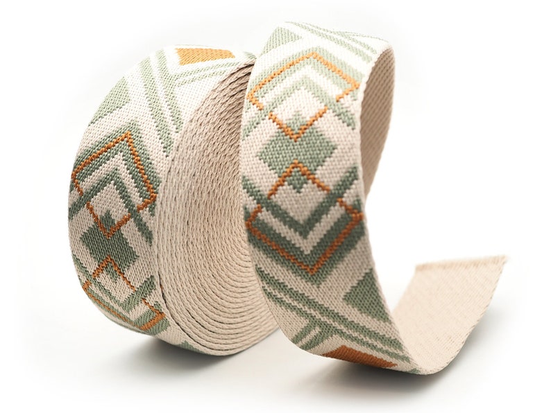 K&ouml;nnte beinhalten: Eine Rolle beiges Stoffband mit einem geometrischen Muster in Gr&uuml;n- und Oranget&ouml;nen. Das Band ist eng gewickelt und zeigt die detaillierte Webart und das Design. Das Muster zeigt Diamanten- und Chevron-Formen.