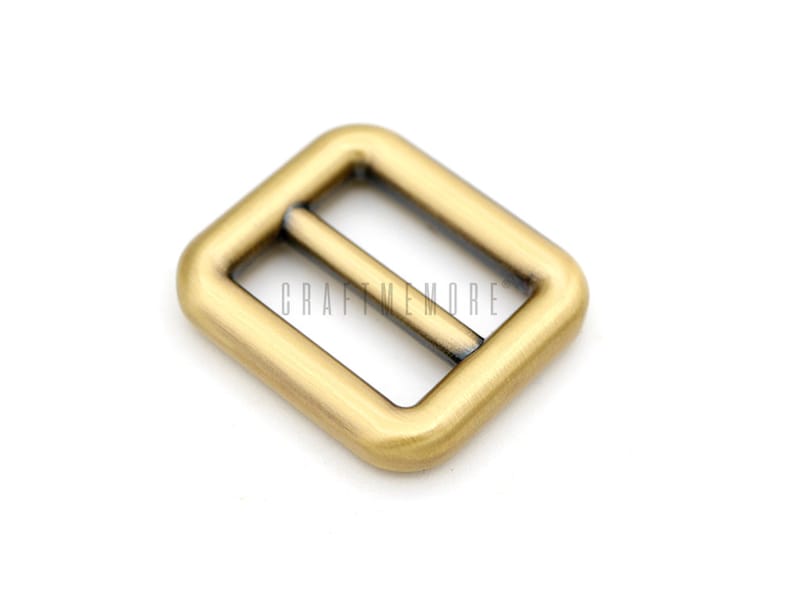 May include: A gold-toned metal buckle with a rectangular shape and a smooth finish. The buckle has two parallel slots for a strap or belt.