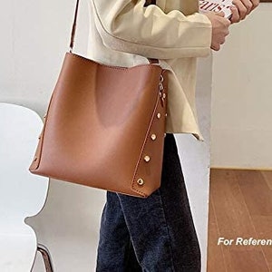 May include: A brown leather tote bag with a shoulder strap and gold accents. The bag has a zipper closure and a spacious interior.