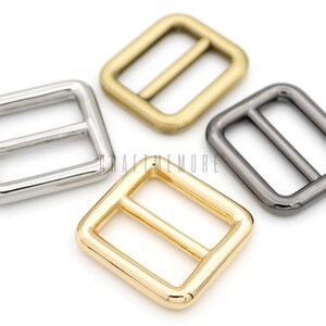 May include: Four metal slider buckles in different finishes: silver, gold, and black nickel. The buckles are square shaped with a rectangular opening and a center bar.
