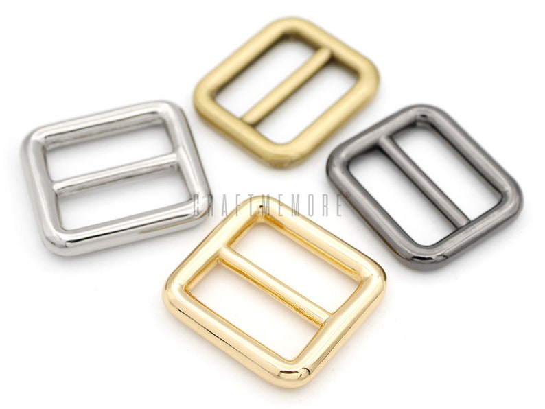 May include: Four metal slider buckles in different finishes: silver, gold, and black nickel. The buckles are square shaped with a rectangular opening and a center bar.