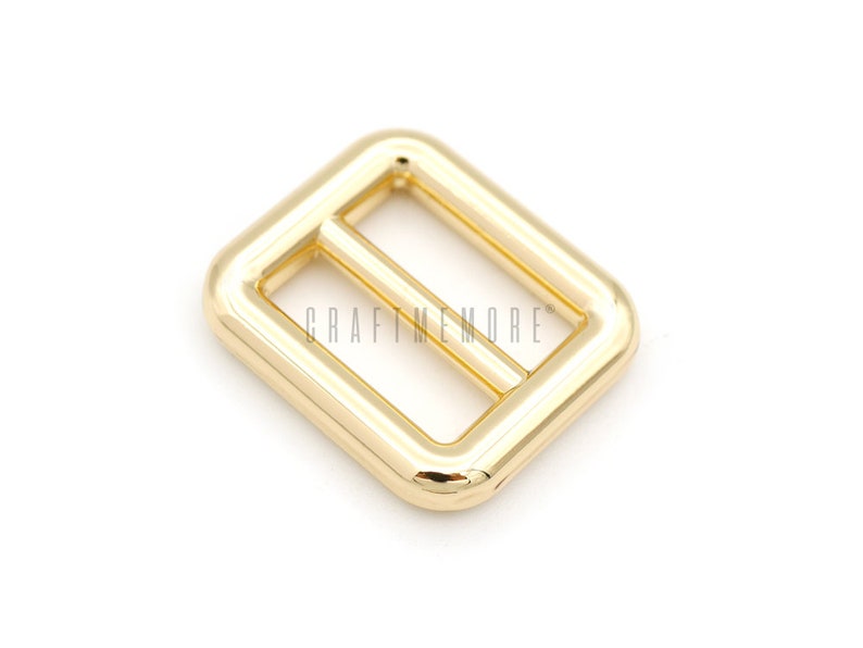 May include: Gold metal buckle with a rectangular shape and a smooth finish. The buckle has a center bar that is slightly raised.