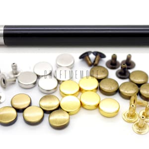 Può includere: Un set di rivetti metallici e uno strumento per fissarli. I rivetti sono di tre colori: oro, argento e bronzo. Lo strumento è nero con una punta argentata.