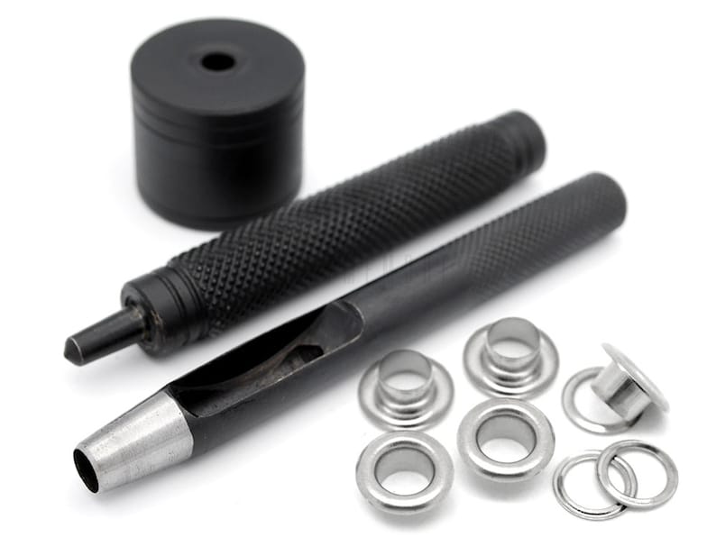 May include: A set of black metal tools for installing eyelets, including a hammer, a punch, and a set of eyelets. The eyelets are silver and come in different sizes.