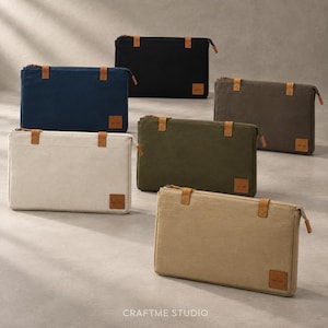 May include: Six rectangular zipped pouches in black, navy blue, cream, olive green, dark grey, and tan. Each pouch features a top zip closure, two tan leather-like tabs at the top corners, and a small square brand label reading CRAFTME STUDIO.