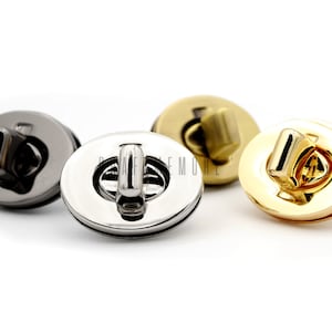 May include: Three metal purse clasps in different finishes: silver, gold, and black. Each clasp has a round, oval-shaped base with a small, raised loop in the center.