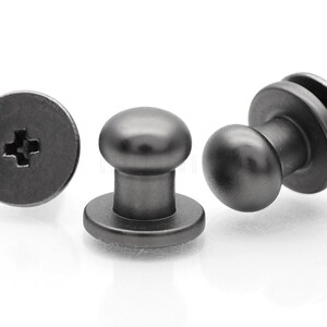 May include: Three black metal push button fasteners. Each fastener has a round head and a flat base with a cross-shaped slot for a screwdriver.