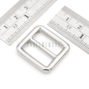 May include: Silver metal buckle with a rectangular shape and a center bar. The buckle is approximately 1 inch wide and 1 inch long.