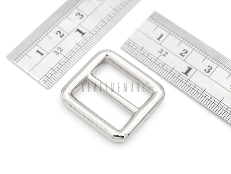 May include: Silver metal buckle with a rectangular shape and a center bar. The buckle is approximately 1 inch wide and 1 inch long.
