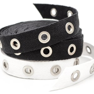 May include: Two rolls of black and white cotton webbing with metal eyelets. The webbing is woven in a herringbone pattern.
