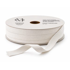 Puede incluir: Un carrete de cinta de espiga blanquecina, con una parte desenrollada. El carrete tiene texto que dice "HANDCRAFTED POSSIBILITIES UNLIMITED CREATIVITY" y "CRAFTMEMORE". Ideal para proyectos de costura y manualidades.