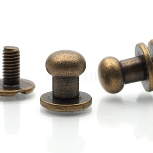 May include: Three antique brass-toned metal button fasteners. Two of the fasteners have a round head and a flat base. The third fastener has a screw head and a flat base.