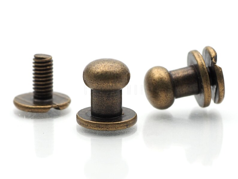 May include: Three antique brass-toned metal button fasteners. Two of the fasteners have a round head and a flat base. The third fastener has a screw head and a flat base.