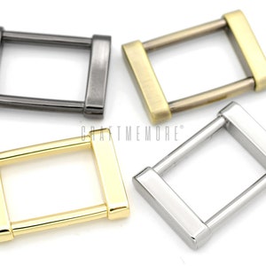 May include: Four metal D-rings in different finishes: silver, gold, antique brass, and black. The D-rings are approximately 2.5 cm in length and width.