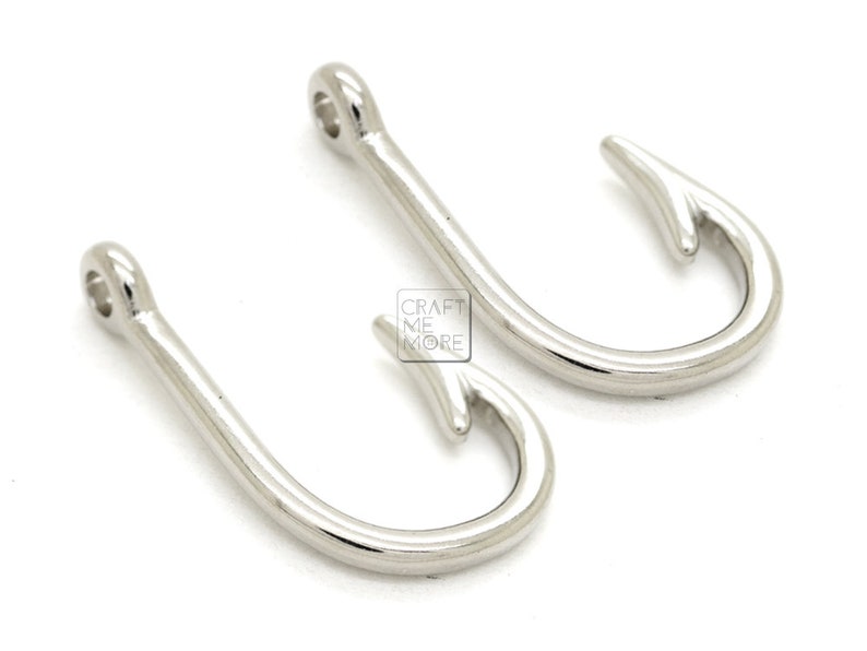 May include: Two silver-toned metal fishing hook charms. The hooks are about 1 inch long and have a smooth, shiny finish.