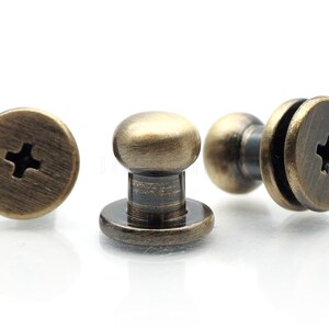 May include: Three antique gold-toned metal screw-on push buttons with a cross-shaped slot in the top.