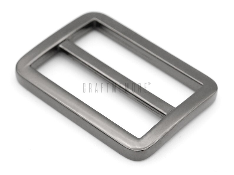 K&ouml;nnte beinhalten: Eine silberfarbene Metallschnalle mit rechteckiger Form und glatter Oberfl&auml;che. Die Schnalle hat eine Mittelstange, die durch die Schlaufe gleitet.