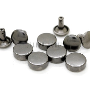 Puede incluir: Primer plano de ocho remaches de metal negro. Los remaches tienen una cabeza redonda y un poste que se puede martillar en su lugar. Los remaches se utilizan comúnmente para unir cuero, tela u otros materiales.