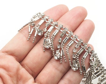 May include: Silver trim with a fringe of clear rhinestones and silver beads. The trim is designed for embellishing clothing or accessories.