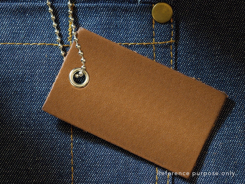 May include: A brown leather tag with a silver metal ring attached to a chain. The tag is on a blue denim background.