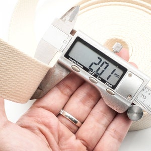 May include: Close-up of a beige cotton webbing roll being measured with a digital caliper. The caliper reads 20.1 mm.